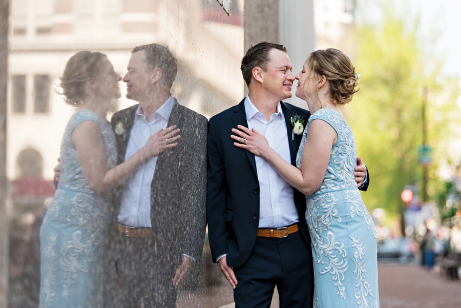 A new bride leaning into her groom for a kiss with their reflection on the wall.